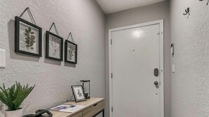 A hallway with a wooden desk, framed artwork, a potted plant, and a white door. - Newly Remodeled 3 BR House w/ Fire Pit, 5 min. From Stadium! (Norman)