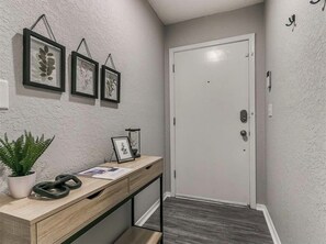 A hallway with a wooden desk, framed artwork, a potted plant, and a white door. - Newly Remodeled 3 BR House w/ Fire Pit, 5 min. From Stadium! (Norman)