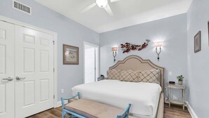 Ein Schlafzimmer mit Bett, Sitzbank, Deckenventilator, Wandleuchten und einer Tür.
