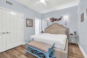 A bedroom with a bed, a bench, a ceiling fan, wall sconces, and a door. - Dunes of Crystal Beach 404 - Beachfront Condo with Community Pool in Destin (Destin)