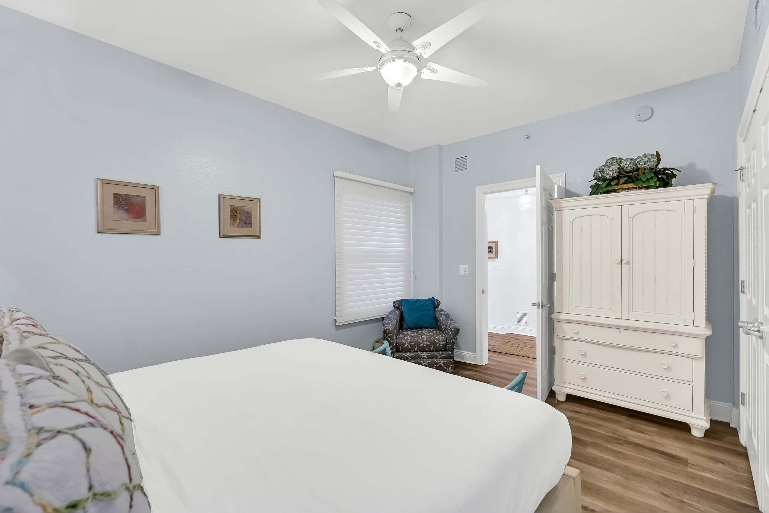 A bedroom with a bed, a ceiling fan, a window with blinds, a chair, and a wardrobe.