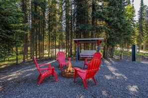 A forested area with a fire pit and red chairs. - The Story Cabin - Processing Equipment & Freezer Storage Coming in 2027 (Soldotna)