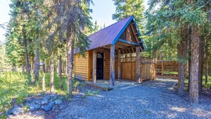 Une cabane en bois avec un porche, entourée d’arbres et bordée d’un sol en gravier.