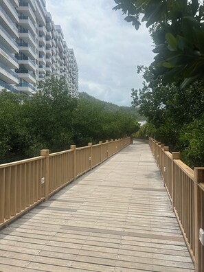A wooden boardwalk with railings, surrounded by greenery and a multi-story building in the background. - Charming 3-bedroom apartment in vibrant Gaira perfect for relaxing (Gaira)