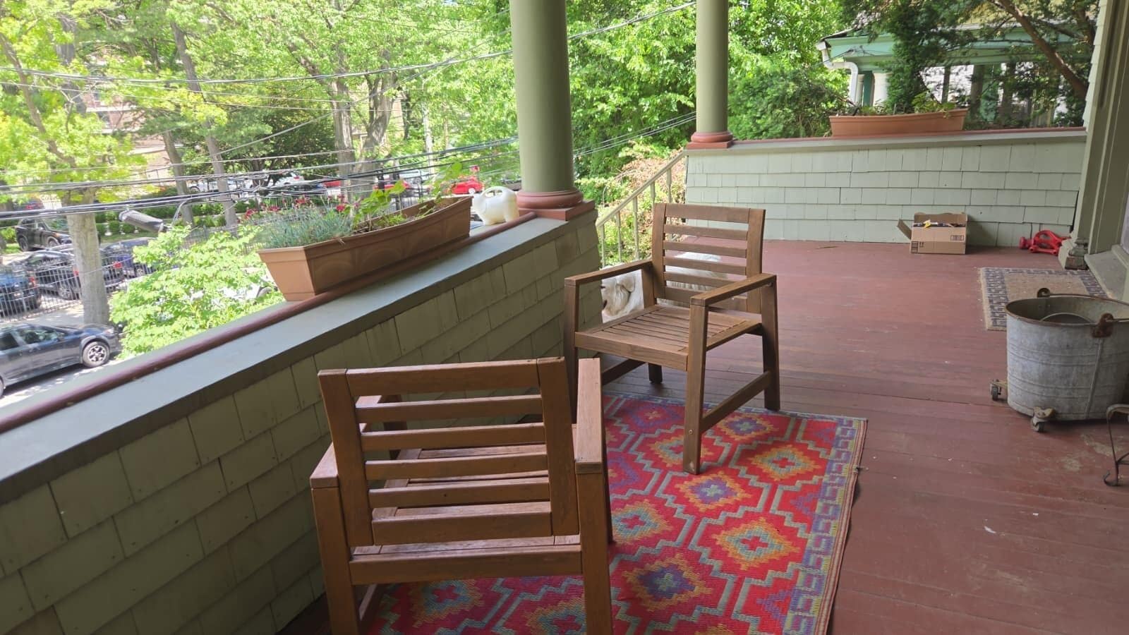 Un balcon avec deux chaises en bois, un tapis coloré et une plante en pot.