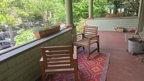 Ein Balkon mit zwei Holzstühlen, einem farbenfrohen Teppich und einem Blumentopf.