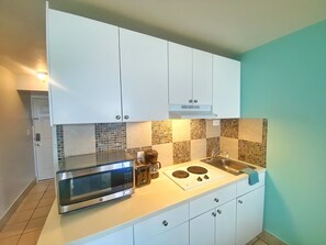 Una cocina compacta con gabinetes blancos, microondas, cafetera y estufa.