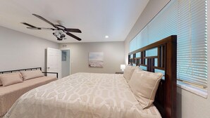 Ein Schlafzimmer mit einem Bett, einem Deckenventilator, einer Tür und einem Fenster mit Jalousien.