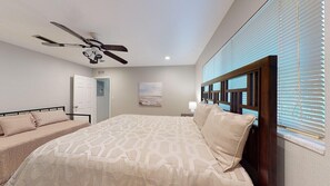 Ein Schlafzimmer mit einem Bett, einem Deckenventilator, einer Tür und einem Fenster mit Jalousien.