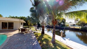 A pool area with a patio, palm trees, and a water body. - Villa by the Sea (Fort Lauderdale)