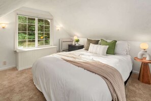 Un dormitorio con un ventanal grande, una cama con ropa de cama blanca, una mesita de noche con lámpara y un equipo de aire acondicionado.