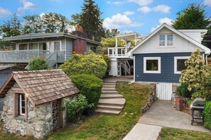 Un barrio residencial con una cabaña de piedra, una estructura de madera con techo inclinado y una casa azul con porche blanco.