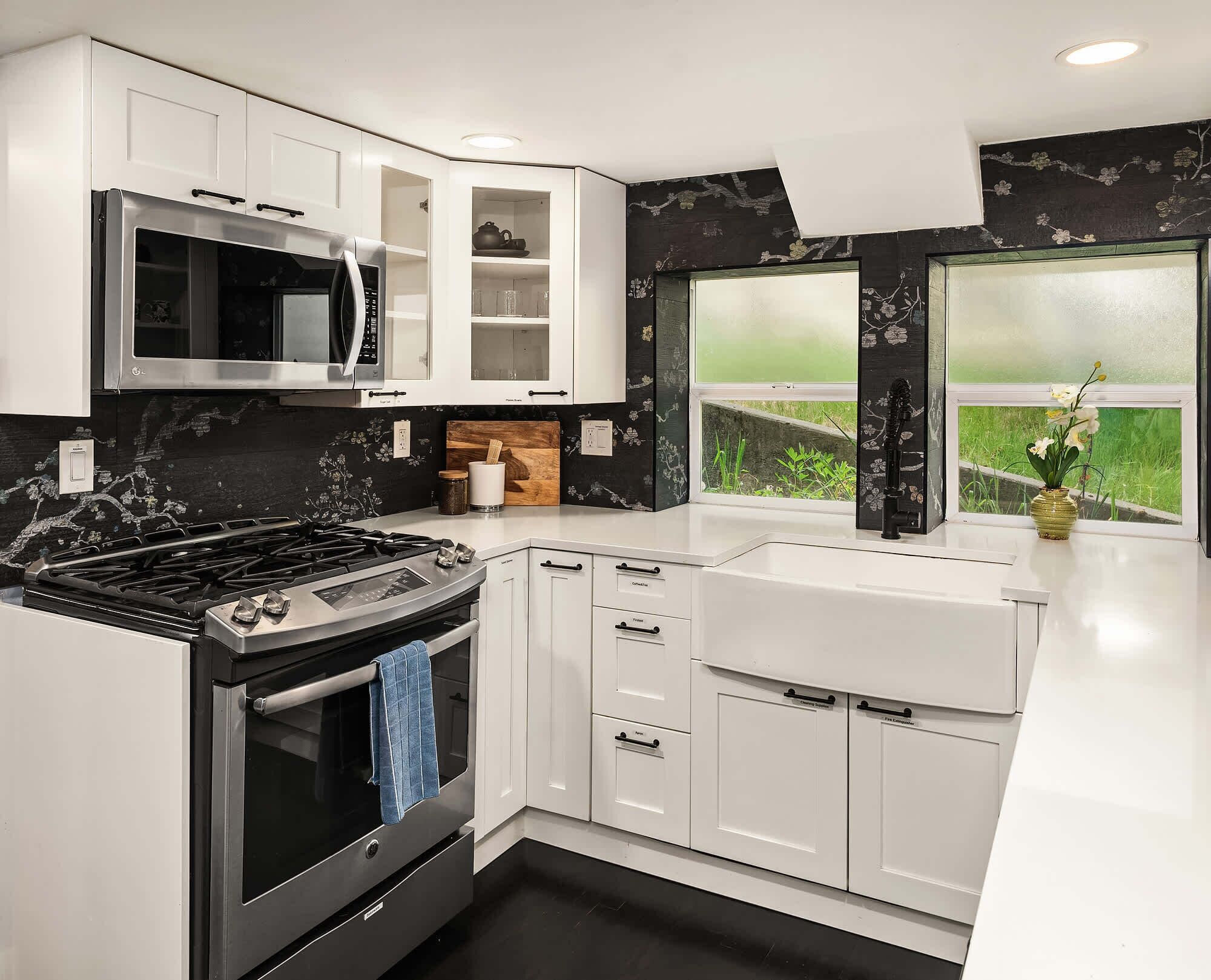 A modern kitchen with white cabinetry, a stainless steel stove, and a window with a view of greenery.