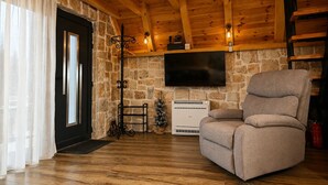 Ein Zimmer mit Holzwandverkleidung, einer Steinsäule, einem Flachbildfernseher, einer Couch und einem Kamin.