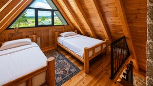 Ein gemütliches Schlafzimmer im Dachgeschoss mit zwei Betten, einem großen Fenster mit Blick ins Freie und einer Holztreppe.
