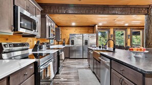 A modern kitchen with stainless steel appliances, wooden cabinetry, and a large island. - Its Got It All Yall by Avantstay Sleeps 27 Indoor Pool + Hot Tub + Theater + Near Pigeon Forge (Pigeon Forge)