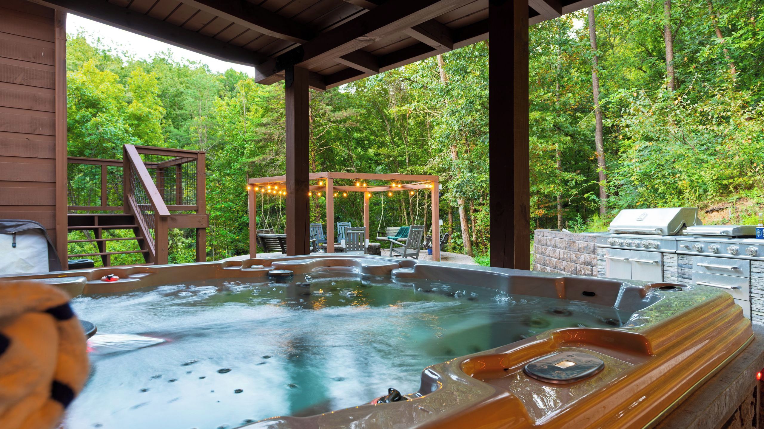 A hot tub area with a wooden pergola, seating, and a grill.