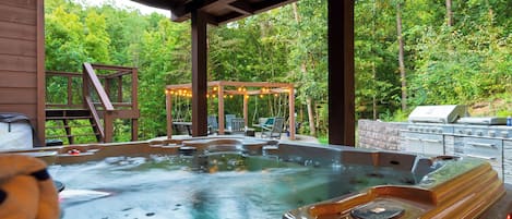 A hot tub area with a wooden pergola, seating, and a grill.