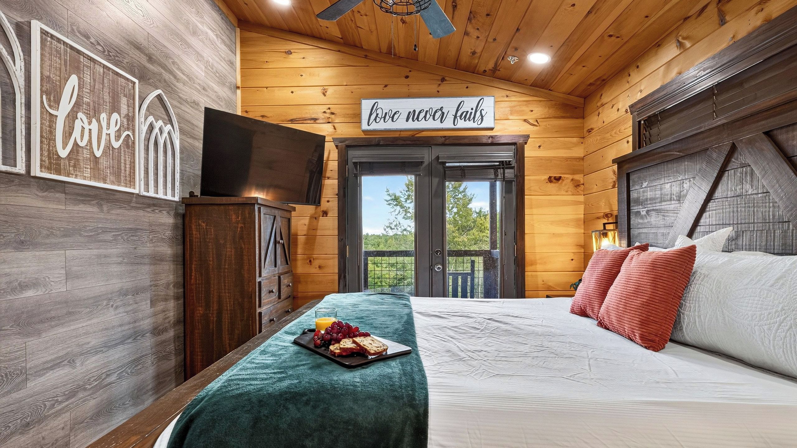 Een slaapkamer in een houten hut met een bed, een ontbijttafel en een bord waarop staat 'liefde faalt nooit'.