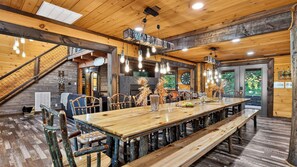 A rustic dining area with a long wooden table, benches, and a staircase leading to an upper level. - Its Got It All Yall by Avantstay Sleeps 27 Indoor Pool + Hot Tub + Theater + Near Pigeon Forge (Pigeon Forge)
