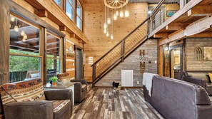 A cozy interior with a wooden staircase, leather sofas, and a view of greenery outside. - Its Got It All Yall by Avantstay Sleeps 27 Indoor Pool + Hot Tub + Theater + Near Pigeon Forge (Pigeon Forge)