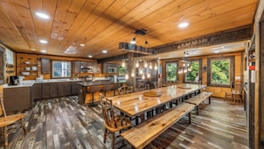 A rustic cabin-style kitchen with wooden floors, a central island, and a dining area with benches. - Its Got It All Yall by Avantstay Sleeps 27 Indoor Pool + Hot Tub + Theater + Near Pigeon Forge (Pigeon Forge)