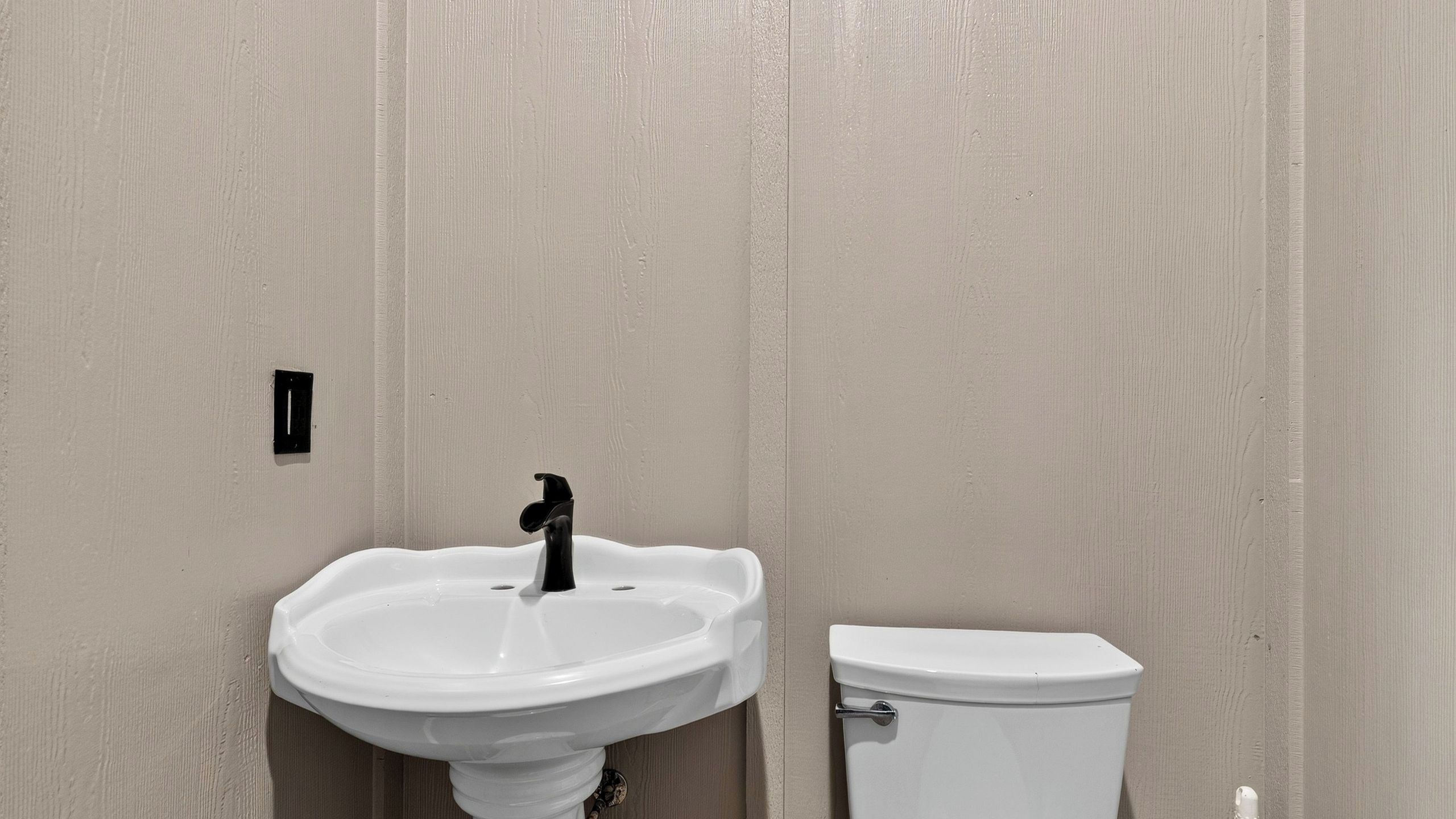 Kylpyhuone, jossa on valkoinen pesuallas ja wc, ja taustalla puinen seinä.