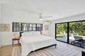 A bedroom with a bed, bedside lamps, a ceiling fan, a window with blinds, and a view of a pool and outdoor chairs. - Villa Terra Mar (Lauderdale-by-the-Sea)