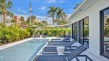 Ein moderner Poolbereich mit Liegestühlen, einem klaren Pool und Blick auf Palmen und Gebäude.