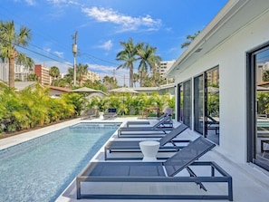 A modern pool area with lounge chairs, a clear pool, and a view of palm trees and buildings. - Villa Terra Mar (Lauderdale-by-the-Sea)