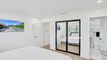 Ein Schlafzimmer mit einem Bett, einer Schiebetür zu einem Badezimmer und Blick auf ein Gebäude.