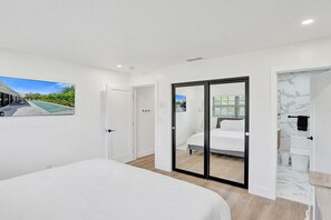 A bedroom with a bed, a sliding door to a bathroom, and a view of a building outside. - Villa Terra Mar (Lauderdale-by-the-Sea)