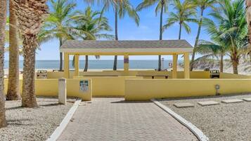 Ein Pavillon am Strand mit freiem Blick auf das Meer, umgeben von Palmen und einem gepflasterten Weg.
