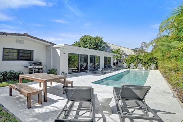 A modern outdoor pool area with lounge chairs, a wooden table, and a barbecue grill. - Villa Terra Mar (Lauderdale-by-the-Sea)