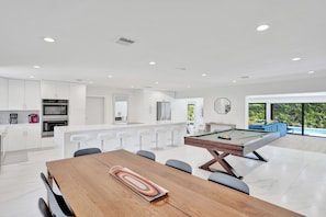 A modern kitchen with white cabinets, a central island with bar stools, and a pool table. - Villa Terra Mar (Lauderdale-by-the-Sea)