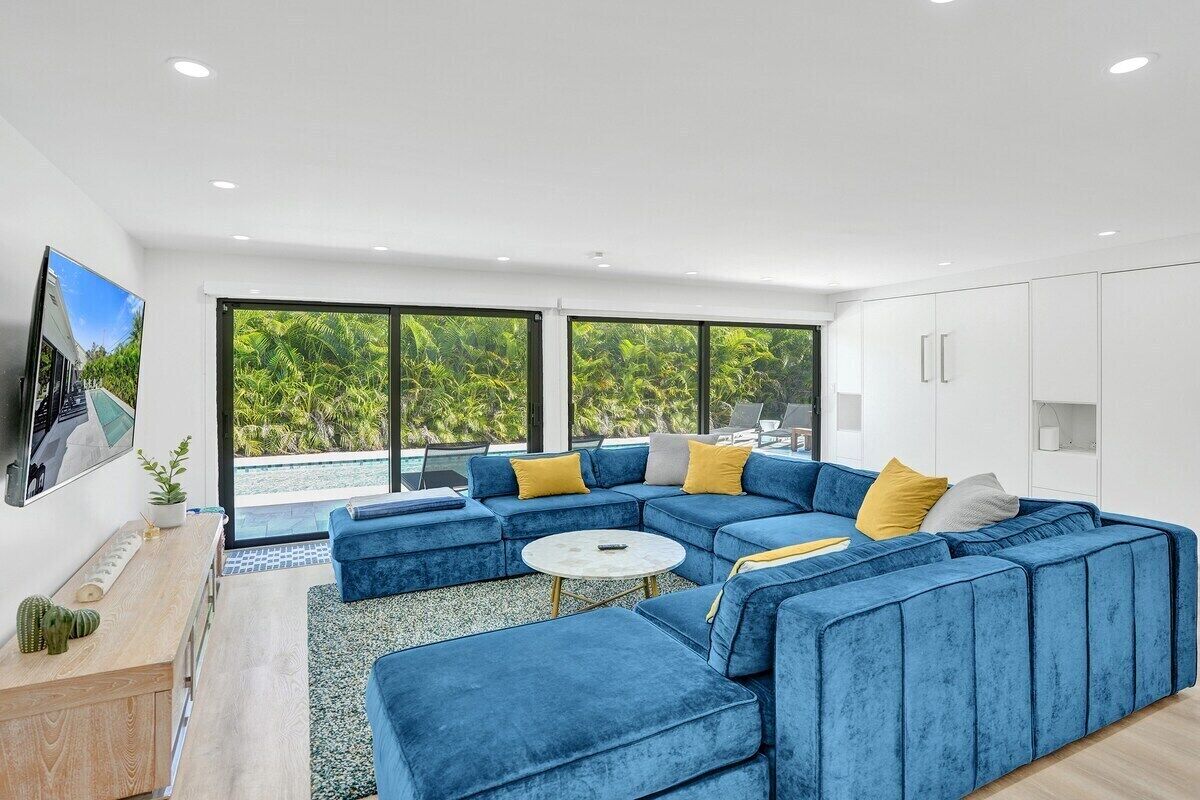 Una sala de estar moderna con un sofá seccional azul, una pequeña mesa redonda de centro y un ventanal con vistas a zonas verdes.