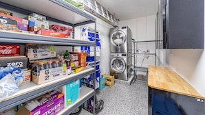 A laundry room with a washing machine, shelves stocked with cleaning supplies, and a wooden counter. - Waters Edge (Lauderdale-by-the-Sea)