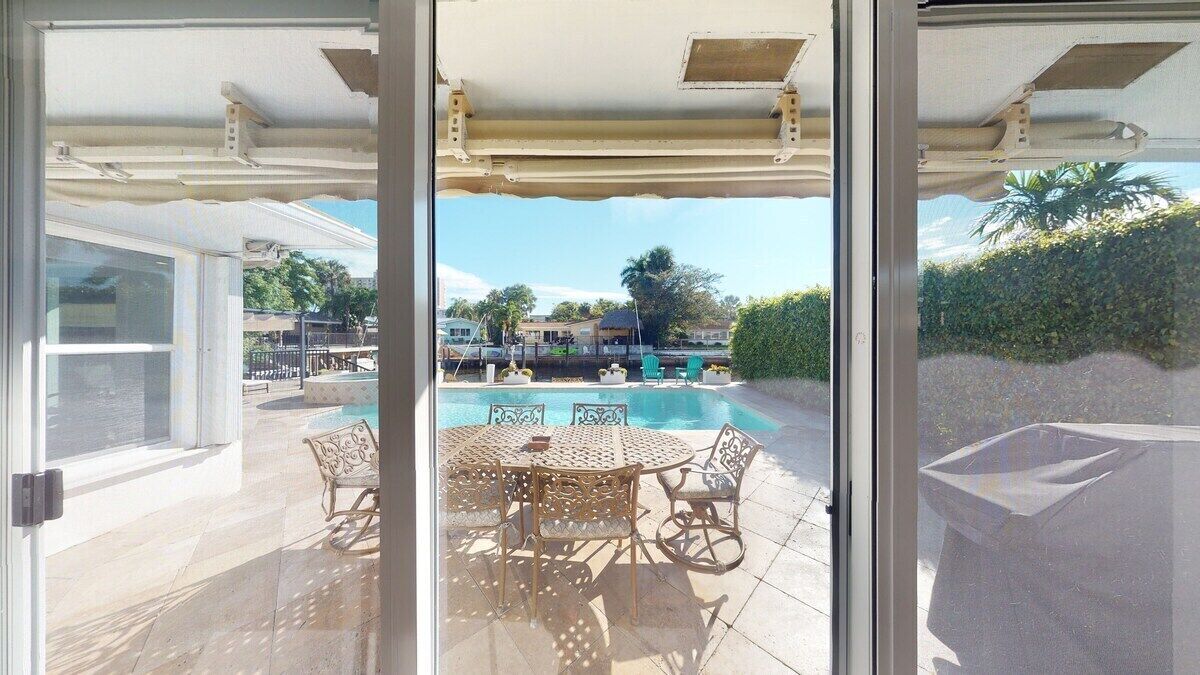 A glass-enclosed patio with a pool, outdoor furniture, and a view of the surrounding area.