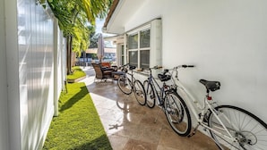 A narrow outdoor corridor with a white wall, a green lawn, and a patio area with a table and chairs. - Waters Edge (Lauderdale-by-the-Sea)