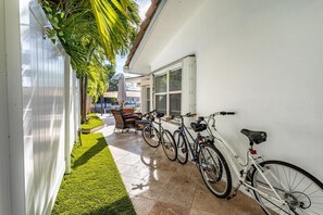 A narrow outdoor corridor with a white wall, a green lawn, and a patio area with a table and chairs. - Waters Edge (Lauderdale-by-the-Sea)