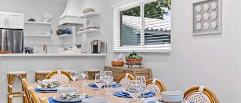 A dining area with a wooden table set for a meal, chairs, and a window with blinds.