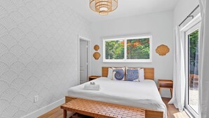 Un dormitorio con cama, un banco, una ventana con persianas y una puerta.