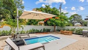 Un patio trasero con piscina, mobiliario exterior y una parrilla.