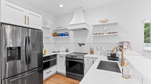 A modern kitchen with stainless steel appliances, white cabinetry, and a central island with a sink. - Al Mare by Avantstay Private Pool + Firepit + Beach Gear Mass Arts District, Near Beach (Fort Lauderdale)