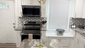 Une cuisine moderne avec des meubles blancs, un plan de travail en marbre, un four encastré et un luminaire suspendu.