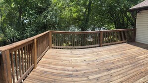 Une terrasse en bois dotée d’une balustrade incurvée, entourée d’une végétation luxuriante.