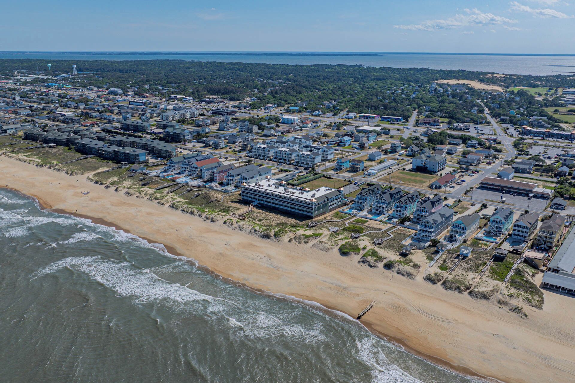 Luftaufnahme einer Küstenstadt mit Strandhäusern, einem großen Hotelkomplex und freiem Blick auf den Ozean.