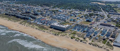 An aerial view of a coastal town with beachfront properties, a large hotel complex, and a clear view of the ocean.