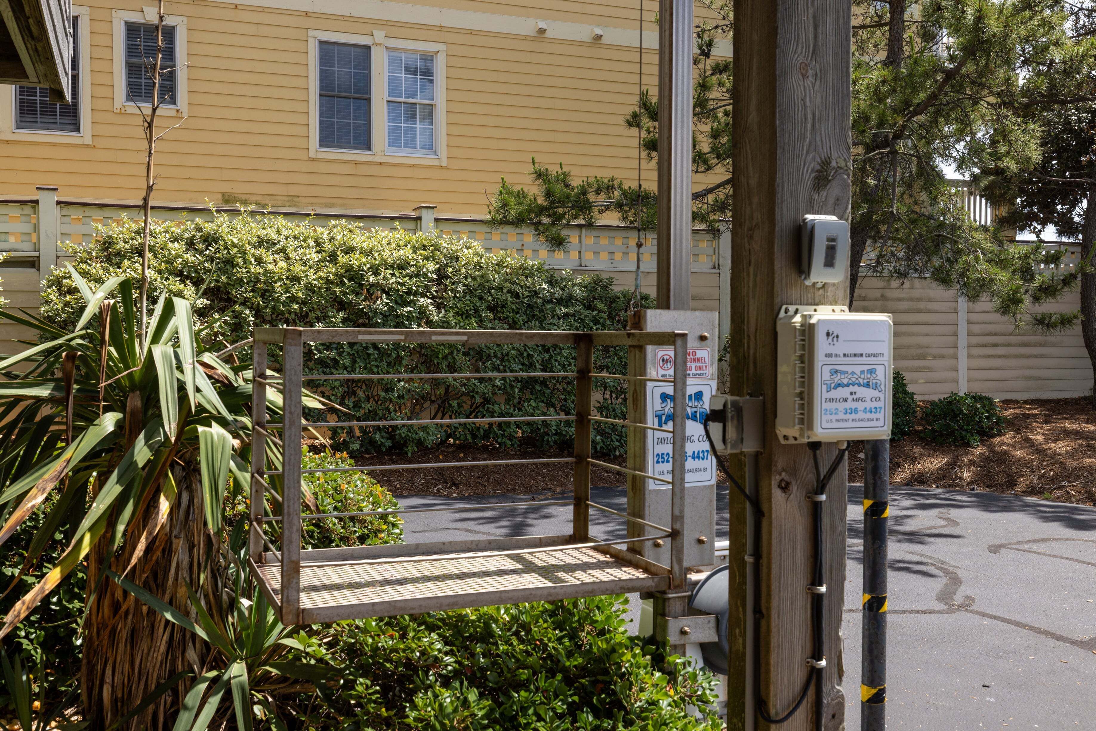 A utility box with a sign, a metal gate, and a yellow building in the background.