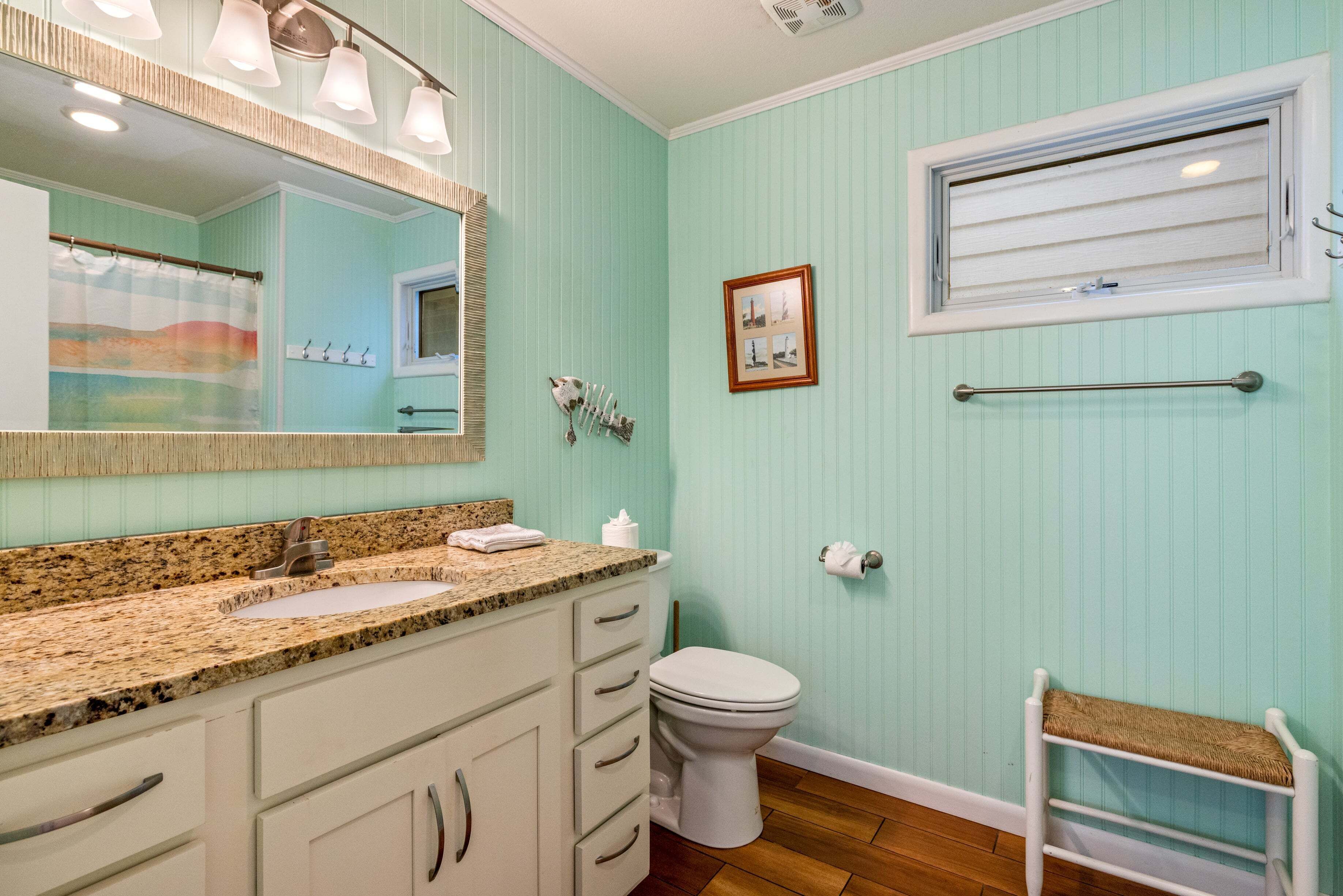 A bathroom with a vanity, sink, mirror, toilet, and a window.